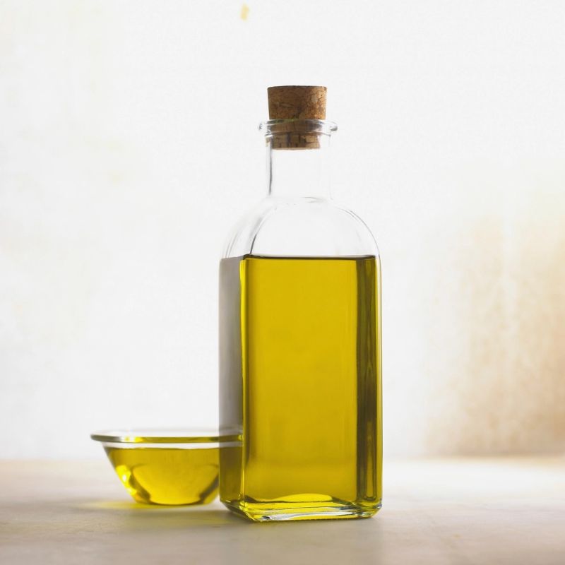 Botella de vidrio con aceite de oliva y un pocillo al lado.